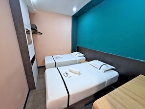 Habitación de hotel con dos camas, una mesa de madera y una pared de acento color verde azulado.
