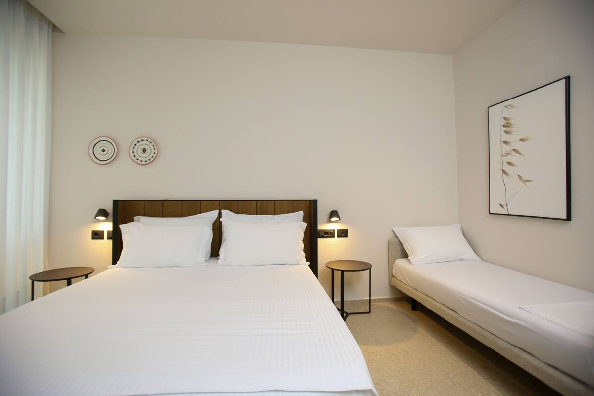 A hotel room with a large bed, a smaller bed, two bedside tables, and wall-mounted lamps.