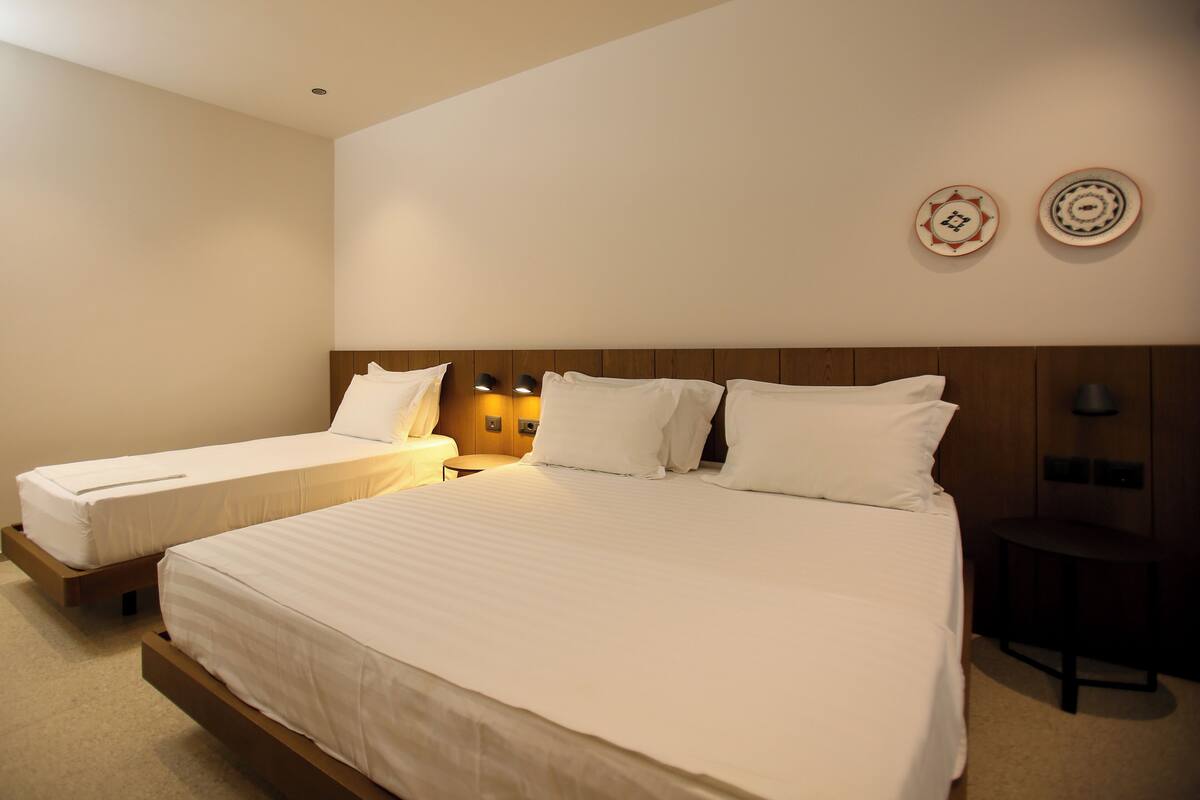 A hotel room with two single beds, a wooden headboard, bedside lamps, and two decorative plates on the wall.