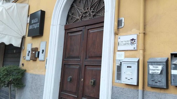Un bâtiment doté d’une grande porte en bois, d’une enseigne indiquant « MAGIA BOUTIQUE » et d’une boîte aux lettres portant le nom de famille.