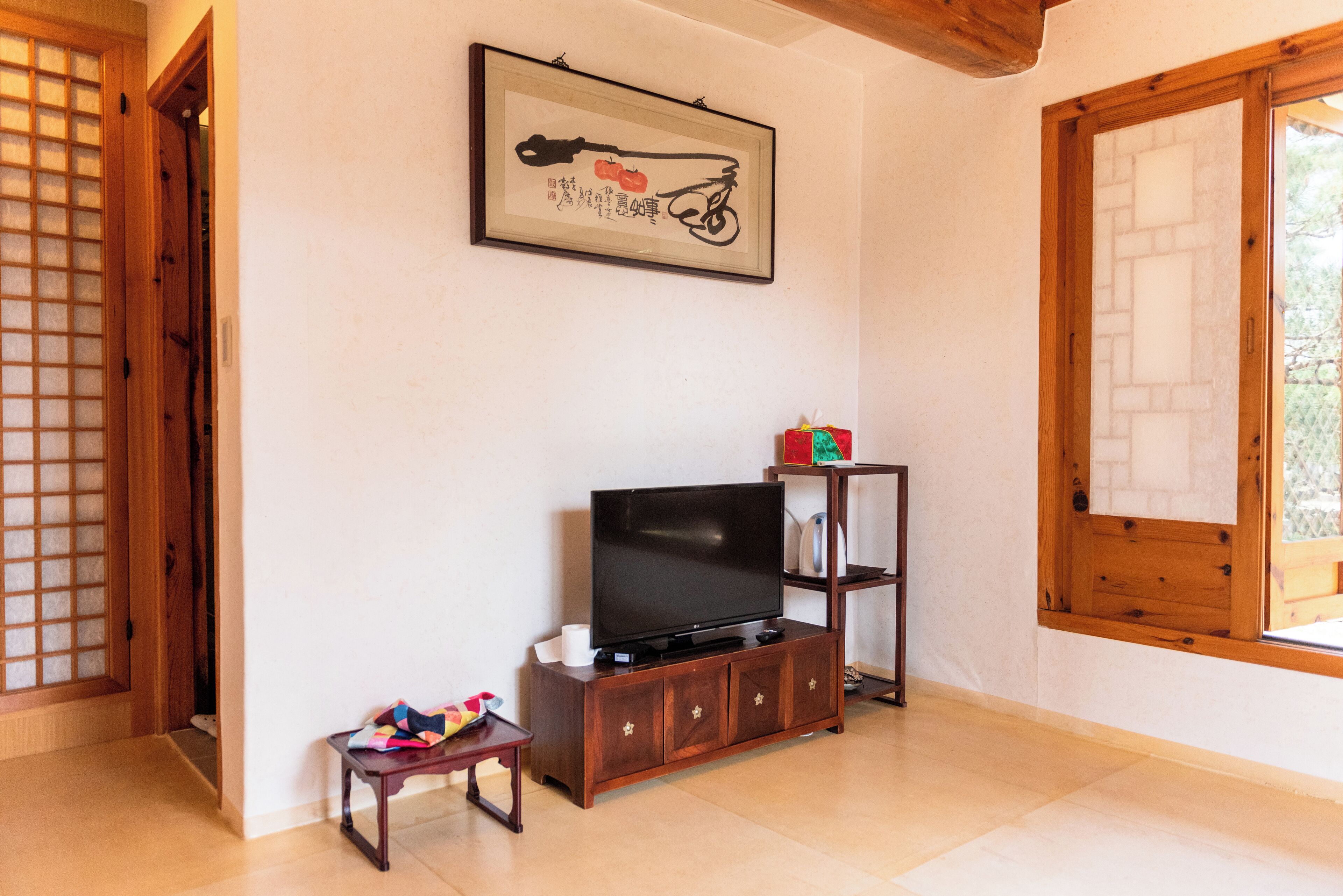 A room with a wooden cabinet under a framed artwork, a television on the cabinet, and a small table with a cloth.