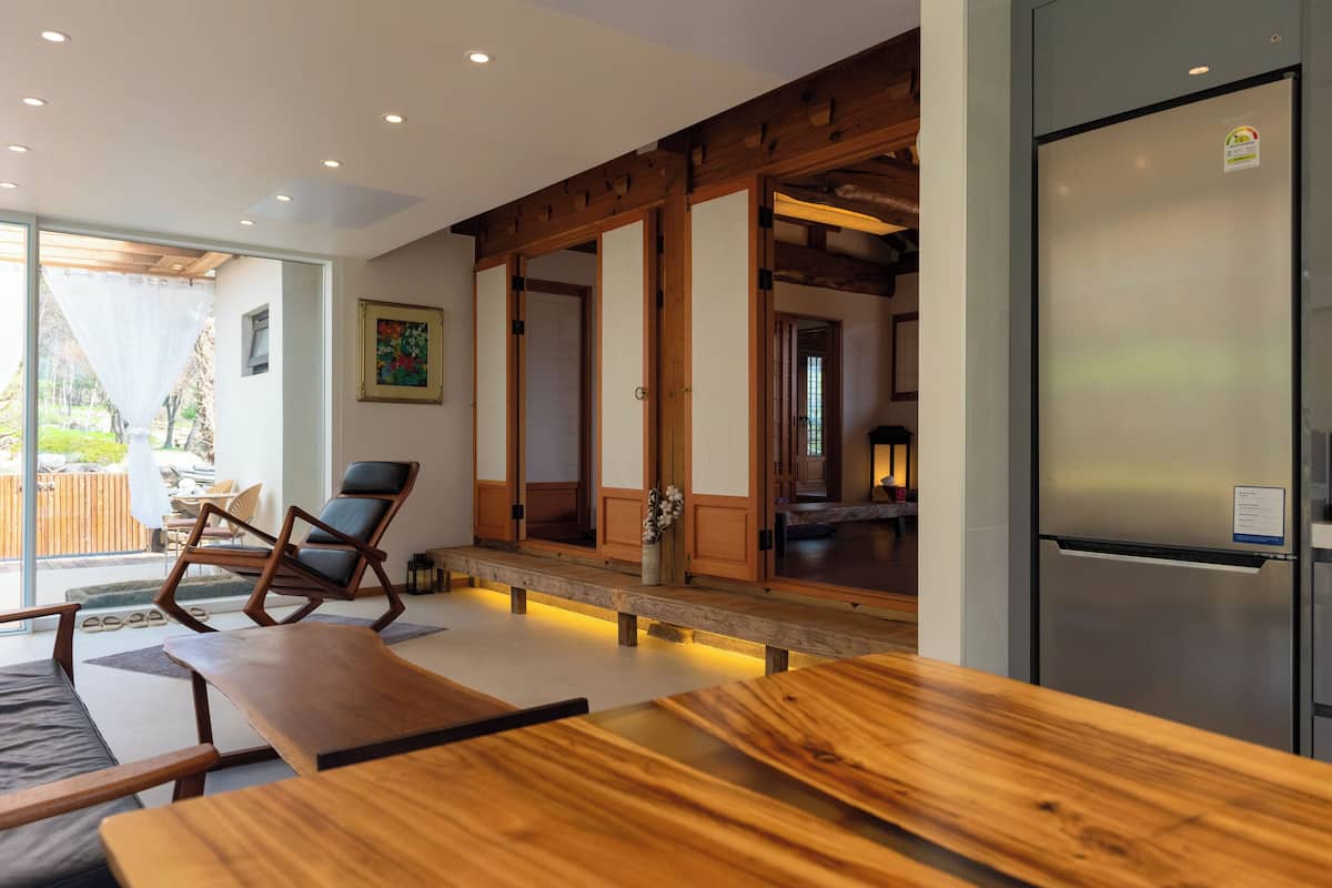 Una cocina moderna con refrigerador de acero inoxidable, piso de madera y una zona de estar con mesa y sillas de madera.