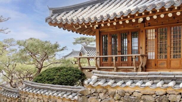 Un edificio tradizionale coreano con tetto in tegole, porte in legno e parete in pietra.