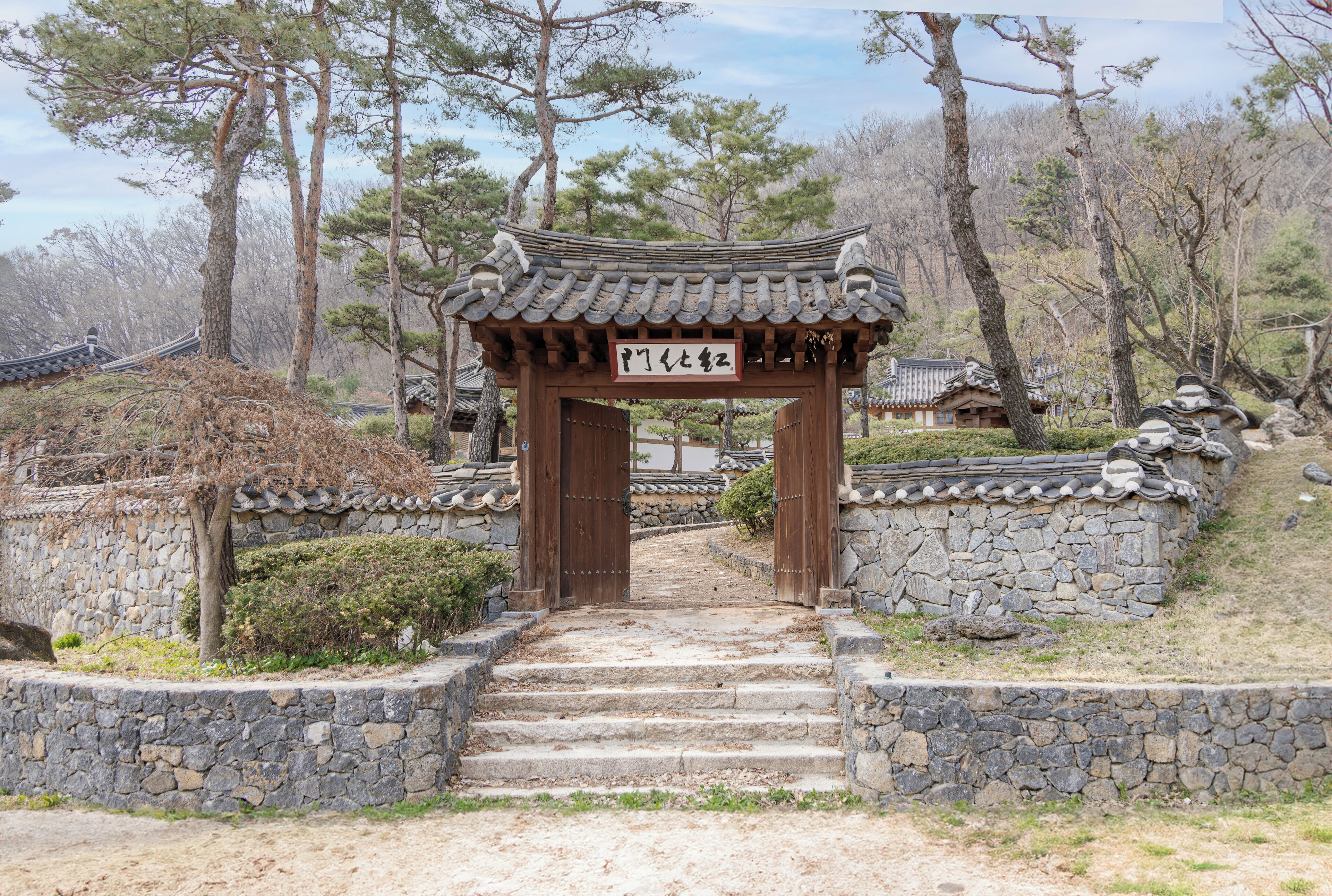 A traditional Korean gate with stone steps leading up to it, surrounded by trees and a stone wall.