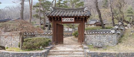 A traditional Korean gate with stone steps leading up to it, surrounded by trees and a stone wall.