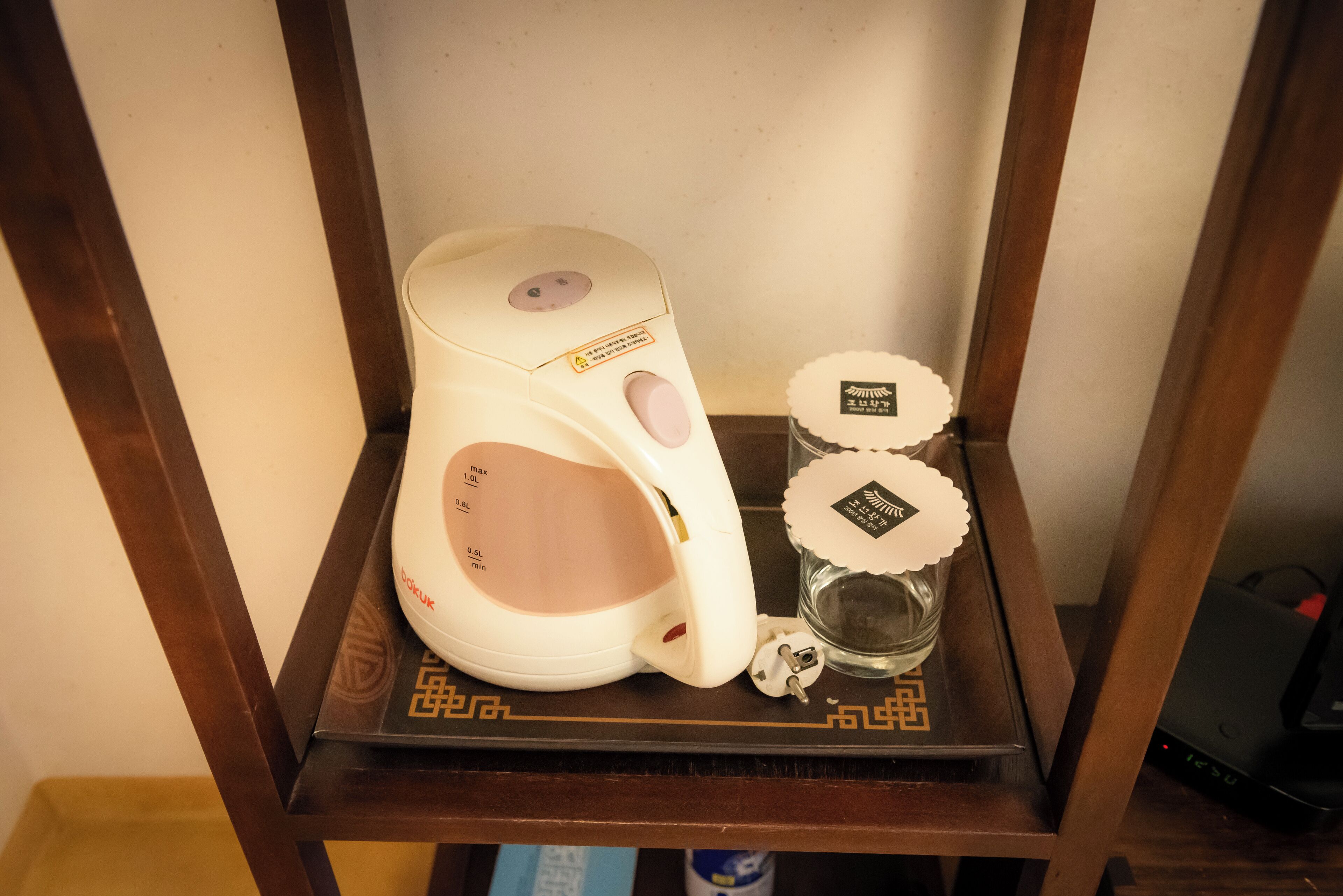 Una tetera eléctrica blanca sobre una estantería de madera con un recipiente de vidrio y un adorno pequeño.