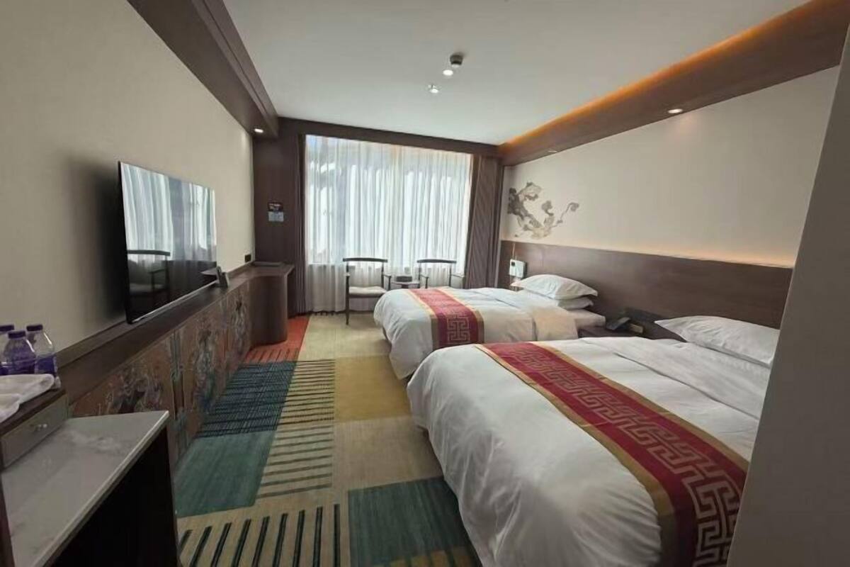 A hotel room with two beds, a TV, a desk, and a window with curtains.