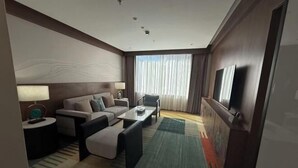 A hotel room with a sofa, armchair, coffee table, and a TV on the wall. - Linzhi Hotel (Nyingchi)