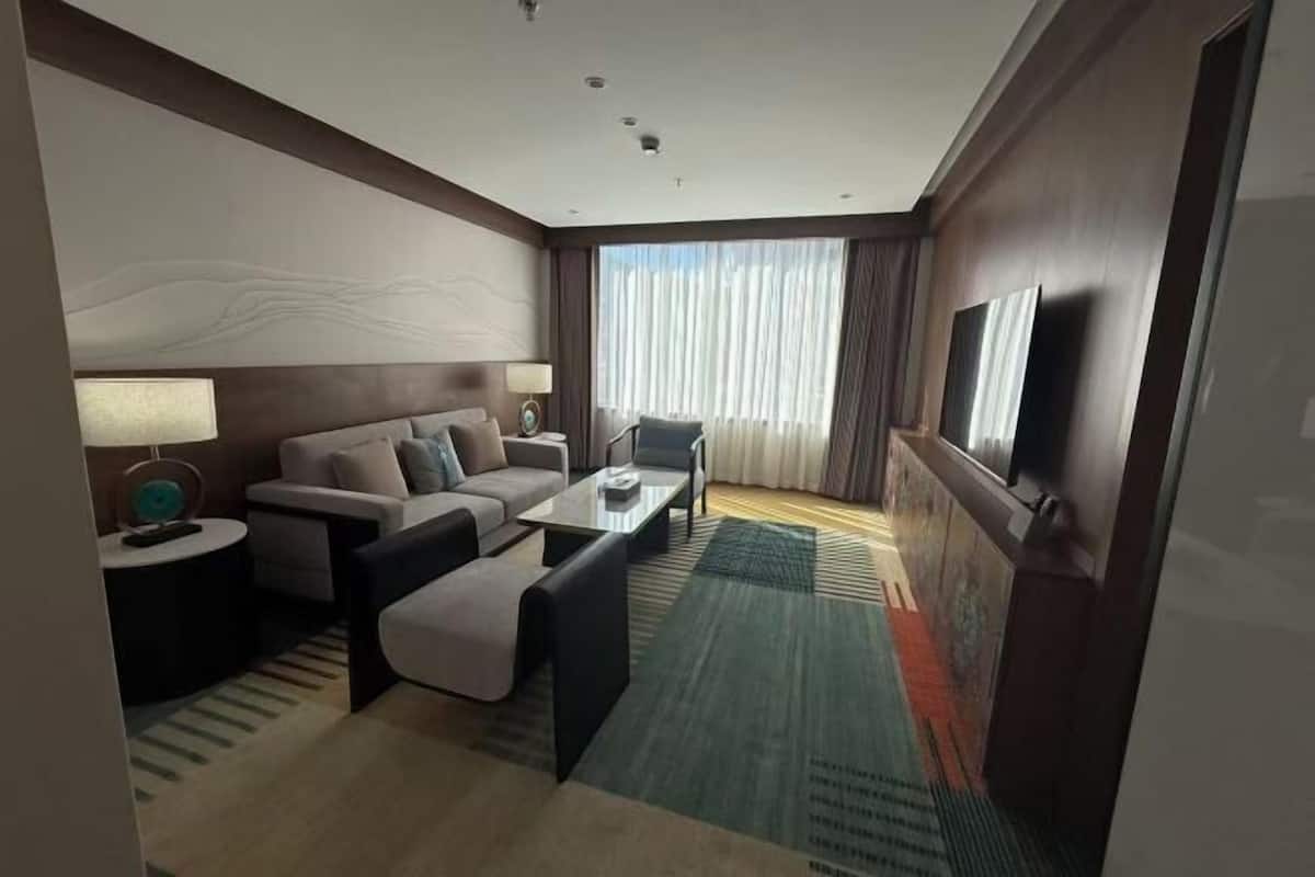 A hotel room with a sofa, armchair, coffee table, and a TV on the wall.