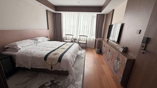 A hotel room with a large bed, two chairs, a small table, a TV, and a decorative cabinet. - Linzhi Hotel (Nyingchi)