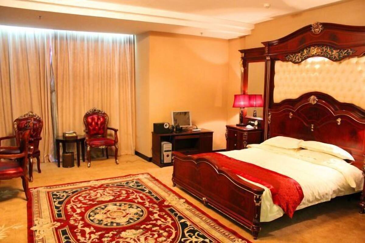A hotel room with a large bed, a wooden headboard, a red carpet, and a desk with a lamp.
