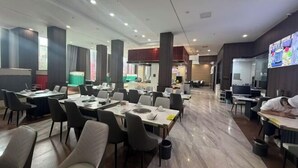 A spacious dining area with multiple tables and chairs, a central column, and a person resting at a table. - Linzhi Hotel (Nyingchi)