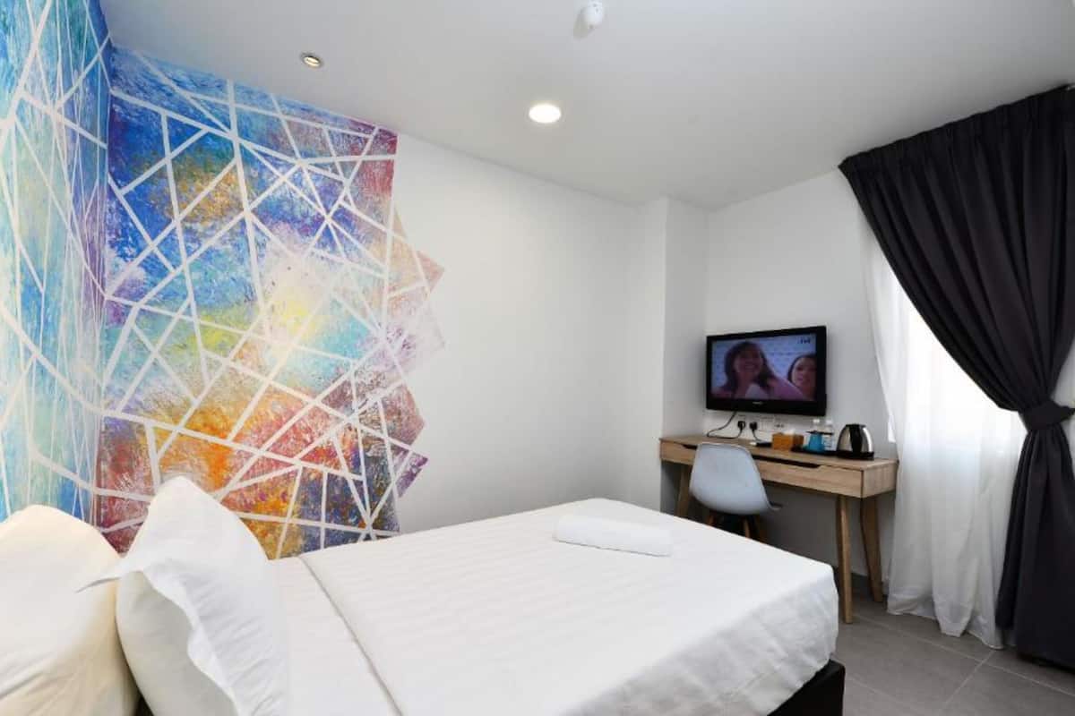 Habitación de hotel con cama, escritorio con computadora, televisor y una obra de arte abstracta y colorida en la pared.