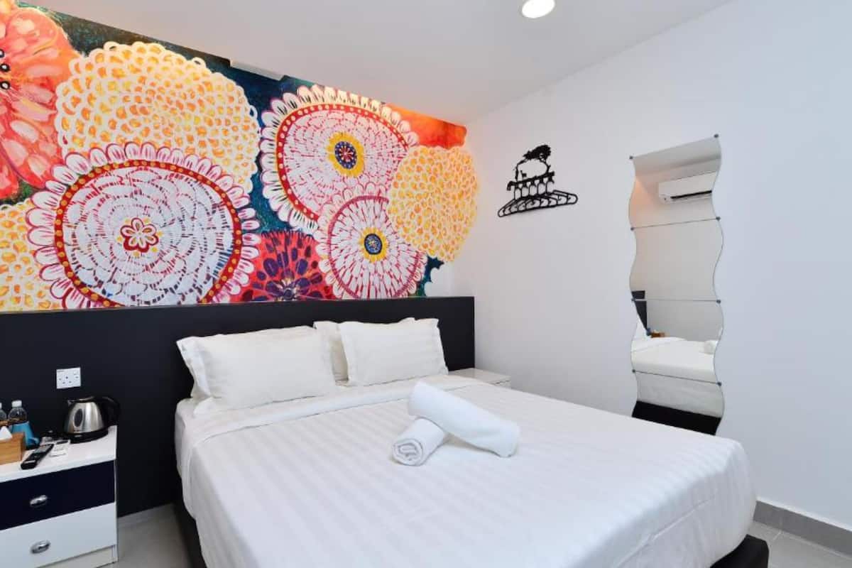Habitación de hotel moderna con una gran obra de arte floral en la pared, una cama bien hecha, una mesita de noche con hervidor y un espejo curvo original.