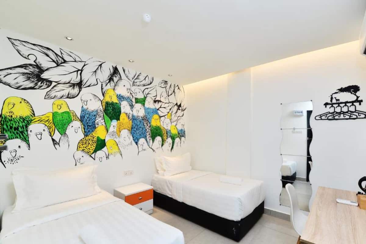 Habitación de hotel con dos camas, un escritorio y un mural de aves en la pared.