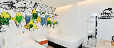 A hotel room with two beds, a desk, and a wall mural of birds.