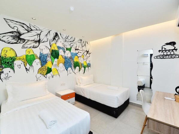 Habitación de hotel con dos camas, un escritorio y un mural de aves en la pared.