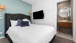 A modern hotel room with a large bed, a flat-screen TV, a bathroom with a vanity and mirror, and a light blue wall. - Currawong - Coastal Bliss - walk to the beach (Rye)