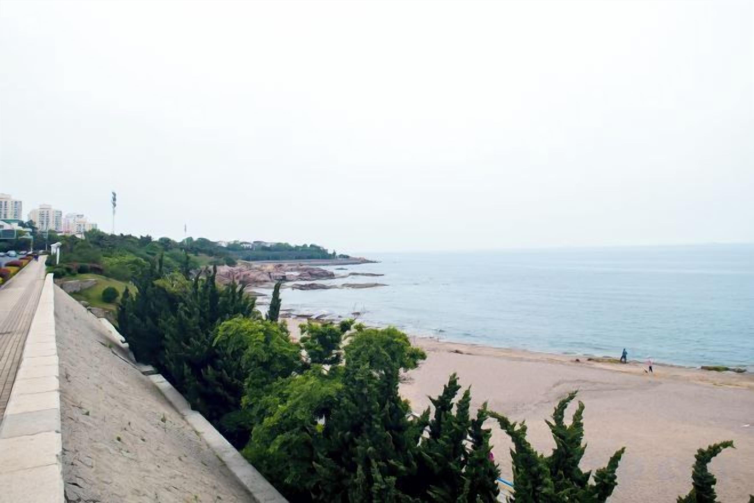 A coastal view with a beach, a promenade, and buildings in the distance.