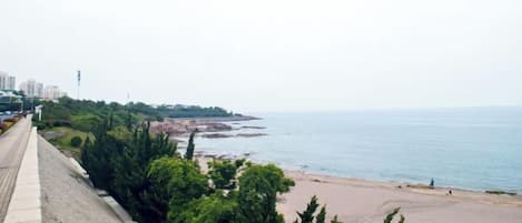 A coastal view with a beach, a promenade, and buildings in the distance.