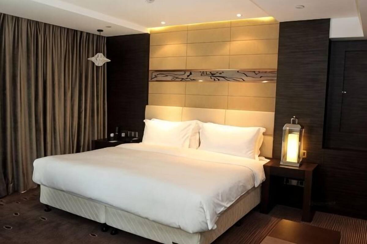 A hotel room with a large bed, a nightstand with a lamp, and a dark wooden headboard.