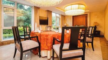 A dining area with a round table, chairs, a chandelier, and a television.