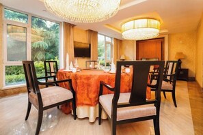 A dining area with a round table, chairs, a chandelier, and a television. - Grand Metropark Qingdao (Qingdao)