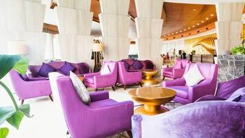 A lobby with purple sofas arranged around a central coffee table, large windows, and a modern ceiling design.