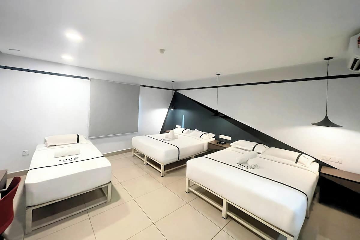 Een moderne, minimalistisch ingerichte hotelkamer met een groot bed, twee kleinere bedden, een bureau en een stoel.