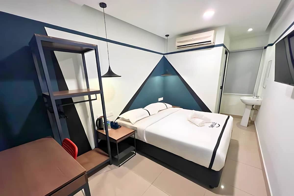 Een moderne hotelkamer met een bed, nachtkastje, lamp en een klein bureau met stoel.