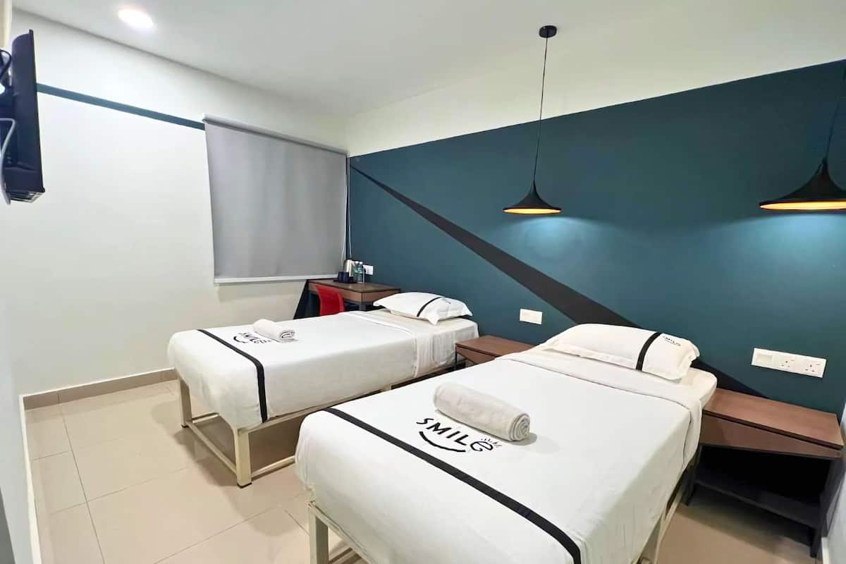 Een hotelkamer met twee bedden, een bureau, een stoel en een raam met gordijnen.