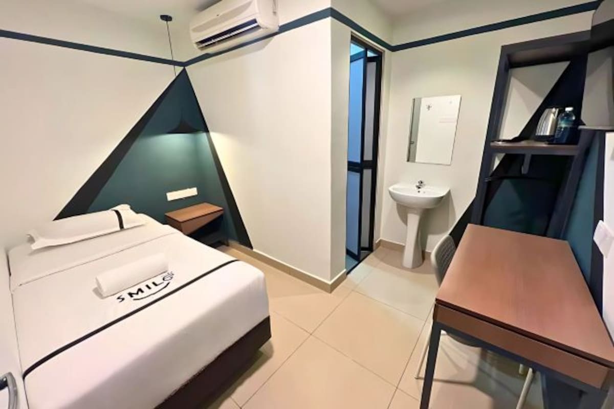 A hotel room with a bed, a small table, a sink, and a mirror.