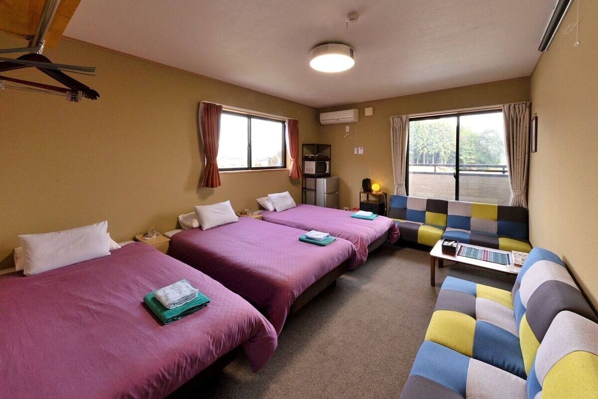 A hotel room with three beds, a sofa, a small table, and a window with curtains.