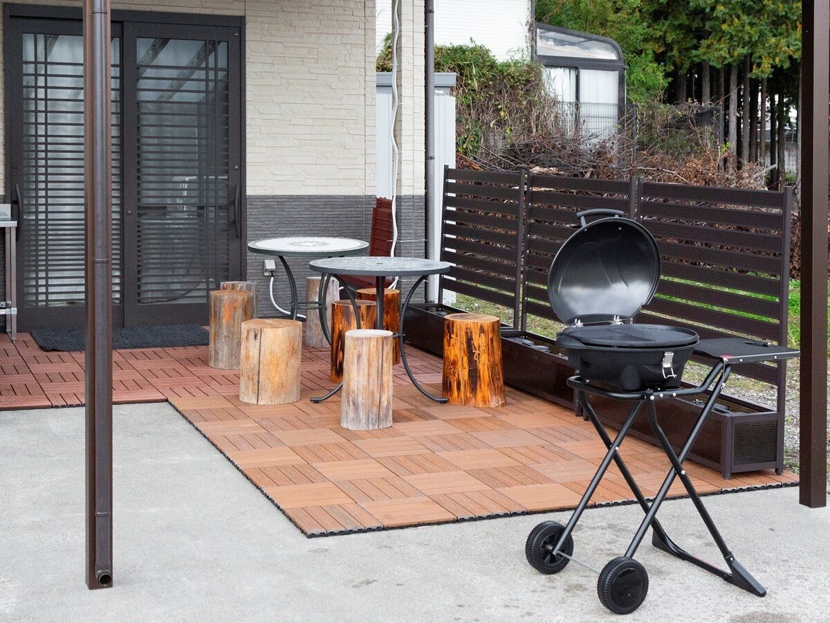 An outdoor patio with a grill, round tables, and wooden stools.