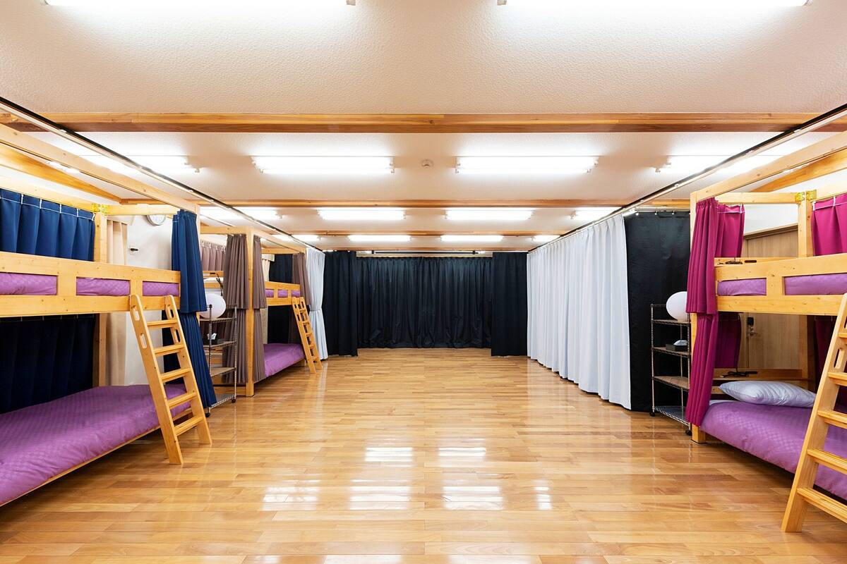 A room with bunk beds, wooden flooring, and curtains.