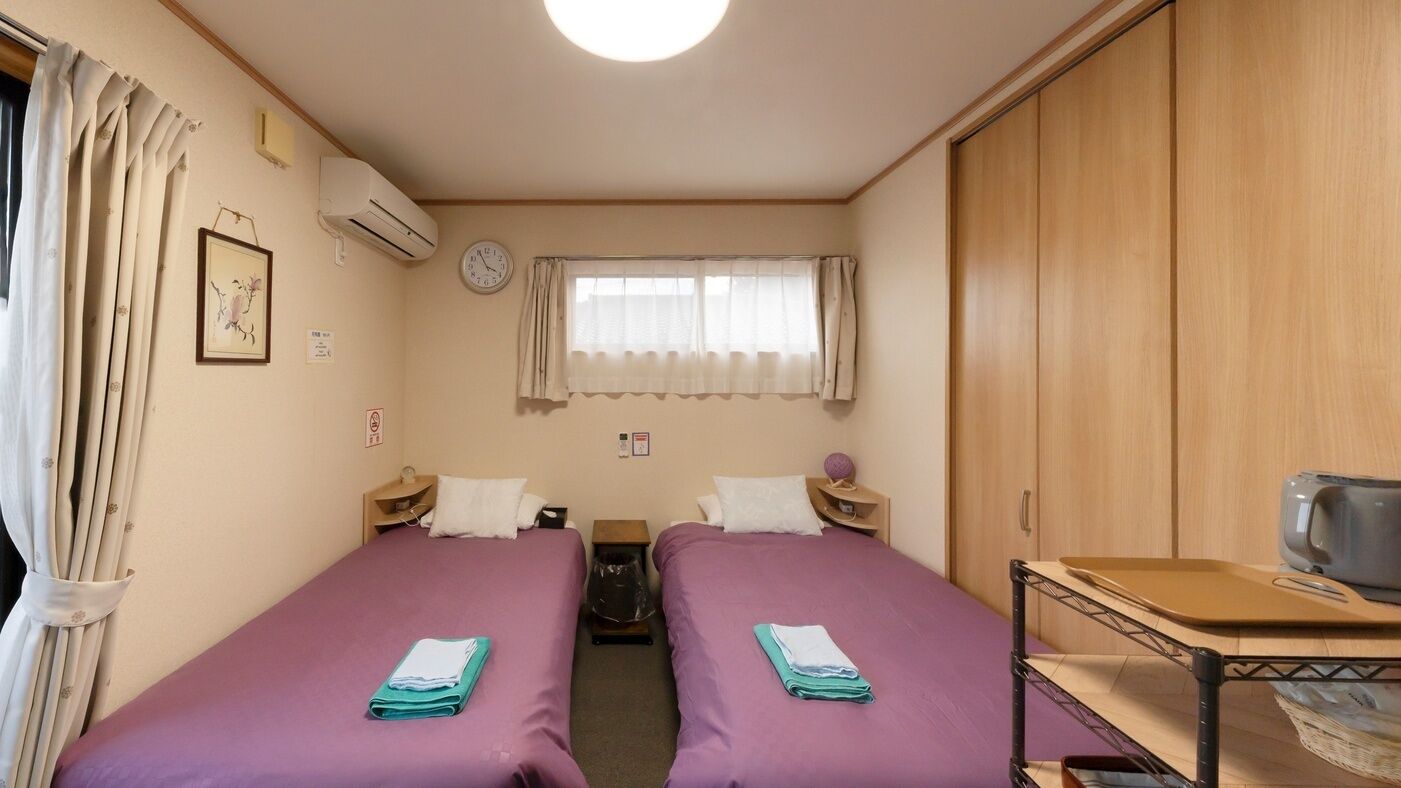 Une chambre avec deux lits, une petite table, une armoire, une horloge et un appareil de climatisation.
