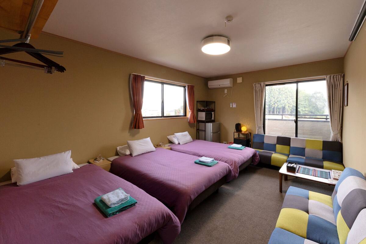 A hotel room with two beds, a sofa, a microwave, and a window with curtains.