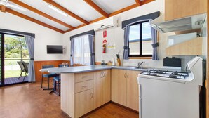 Eine moderne Küche mit Holzschränken, einem Gasherd, einem Flachbildfernseher und einem Essbereich mit Tisch und Stühlen.