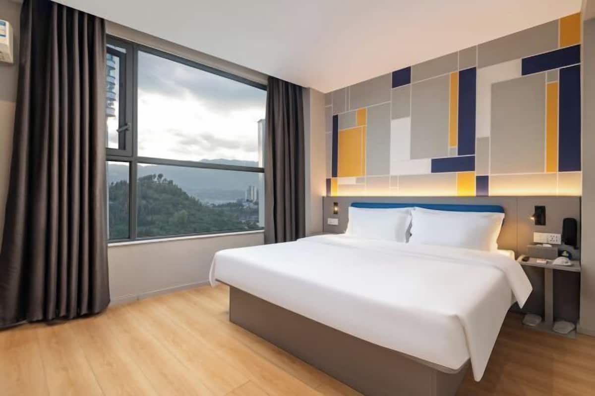 A modern hotel room with a large bed, a view of a cityscape, and a geometric wall design.