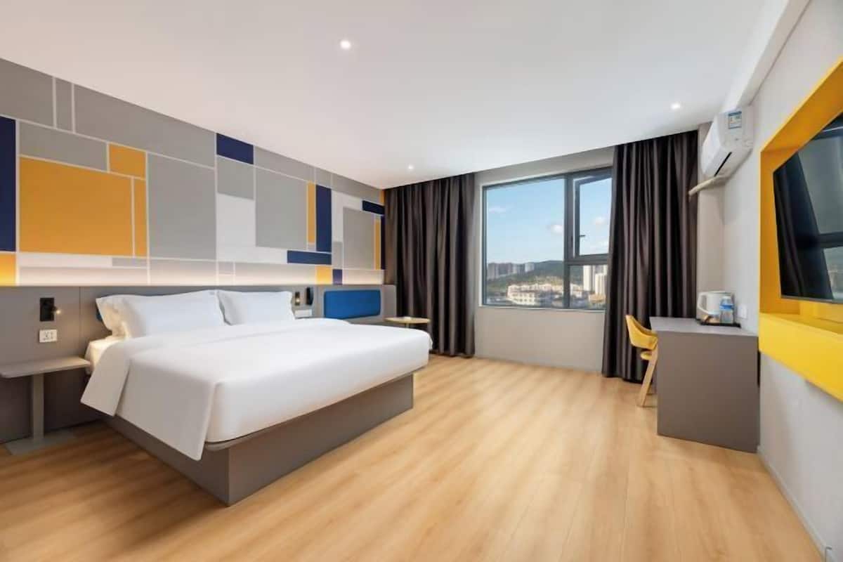 A modern hotel room with a large bed, a desk, and a view of the city.