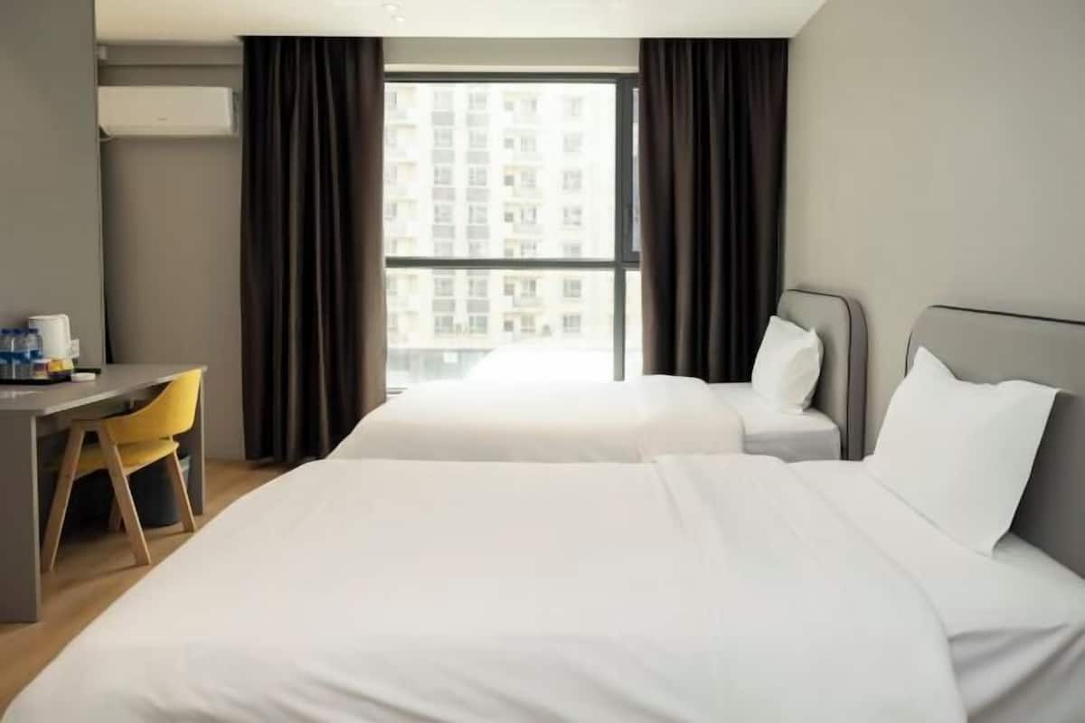 A hotel room with two beds, a desk, a chair, and a large window with curtains.