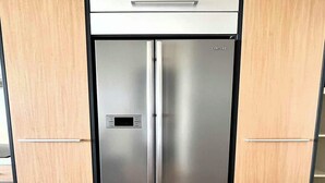 Un refrigerador Samsung de acero inoxidable con diseño de panel de madera, ubicado en una cocina moderna con armarios y piso de madera.