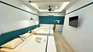 Habitación de hotel con tres camas, ventilador de techo, televisor y piso de madera.
