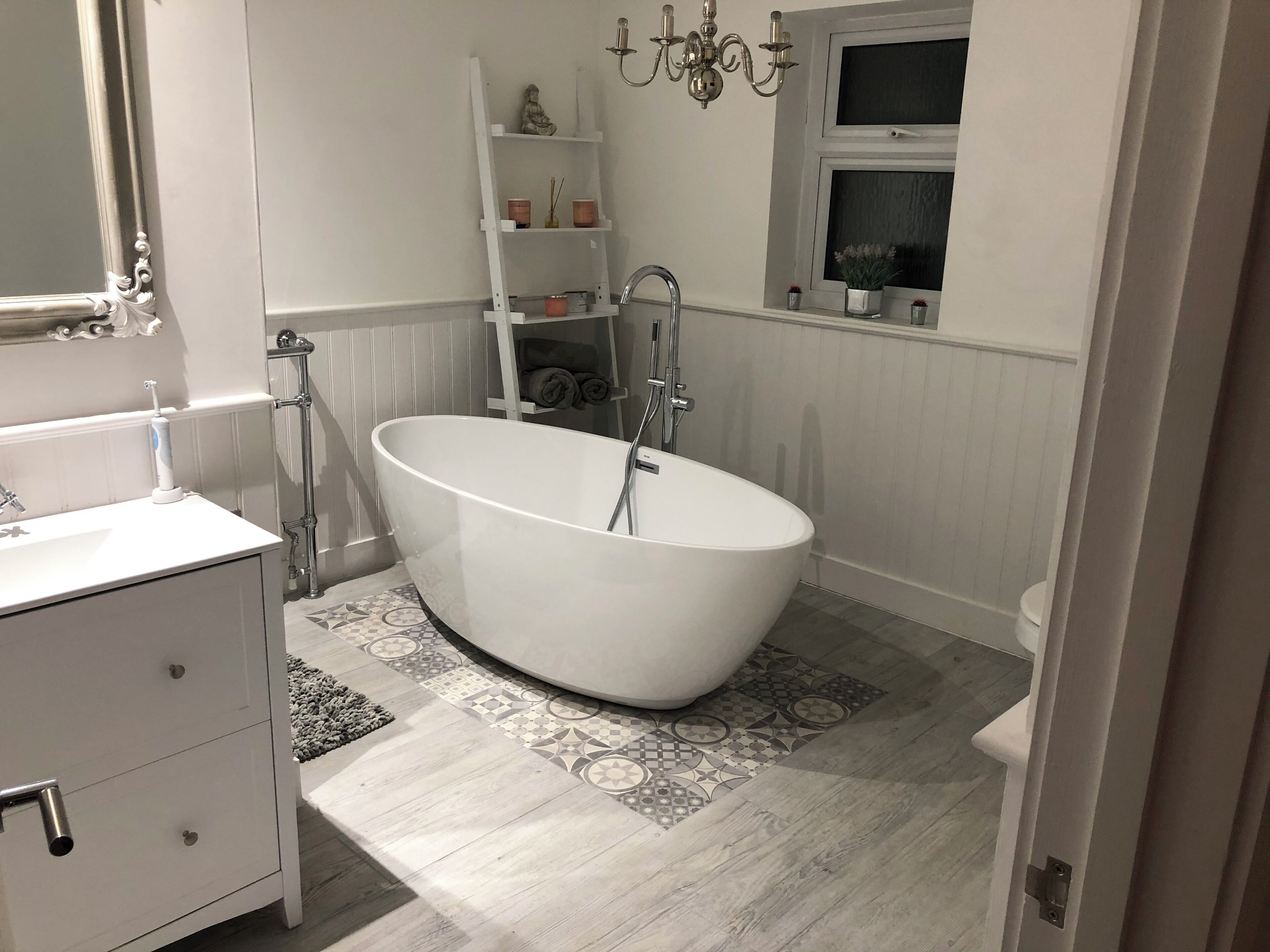 A modern bathroom with a freestanding bathtub, a white vanity with a mirror, and a patterned floor.
