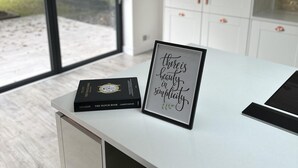 Une cuisine moderne avec un plan de travail blanc, une citation inspirante encadrée et un livre sur les montres.