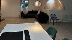 Une cuisine moderne dotée d’une verrière, de luminaires suspendus, d’un coin repas et d’un espace salon confortable avec un canapé et des fauteuils.