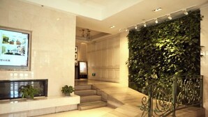 A hotel lobby with a marble reception desk, a staircase, and a wall of green foliage.