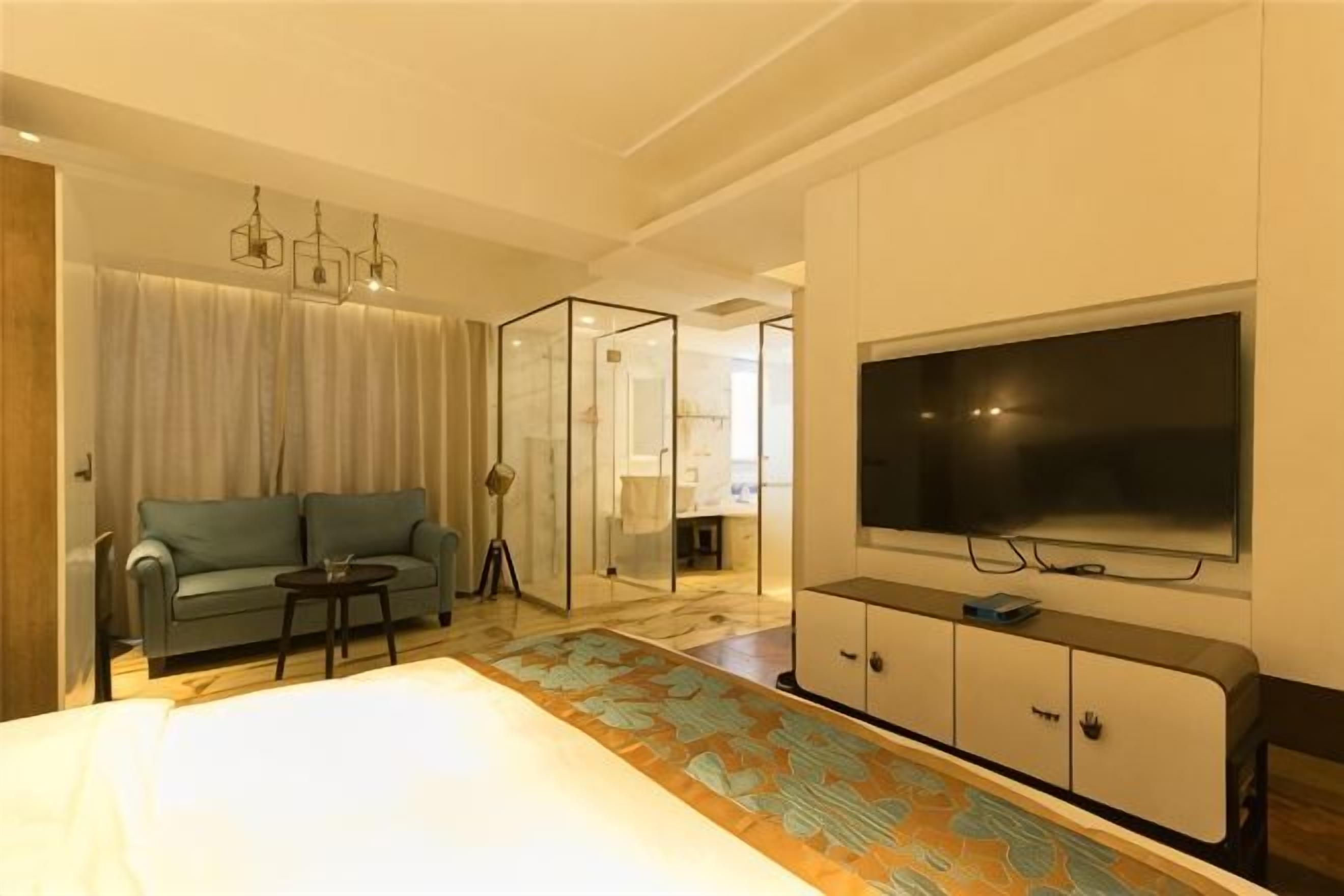 Quarto de hotel com sofá, televisão, divisória de vidro e piso estampado.