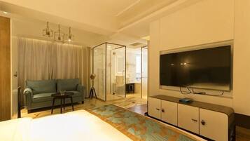 Quarto de hotel com sofá, televisão, divisória de vidro e piso estampado.