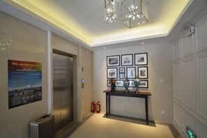 Una hall d'albergo con ascensore, una reception, quadri appesi al muro e un estintore.